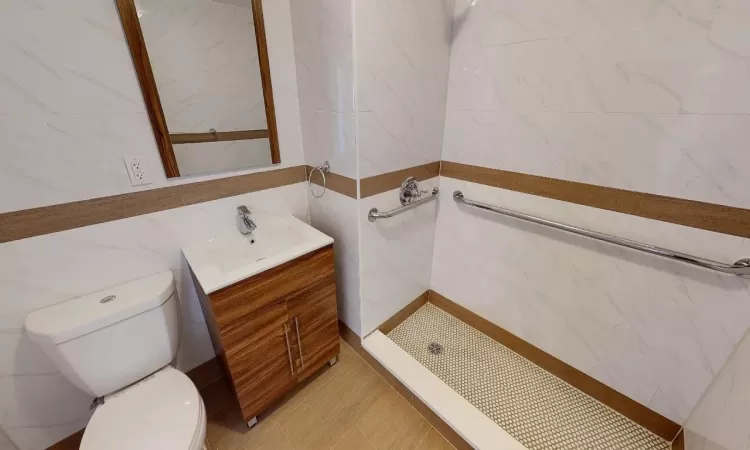 Bathroom with walk in shower, tile patterned floors, toilet, vanity, and tile walls