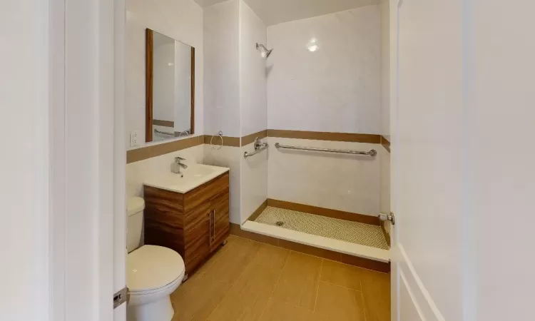 Bathroom featuring vanity, toilet, tile walls, and a tile shower