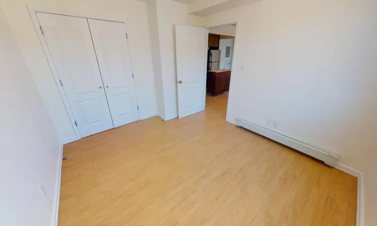 Unfurnished bedroom featuring stainless steel fridge, light hardwood / wood-style floors, baseboard heating, and a closet