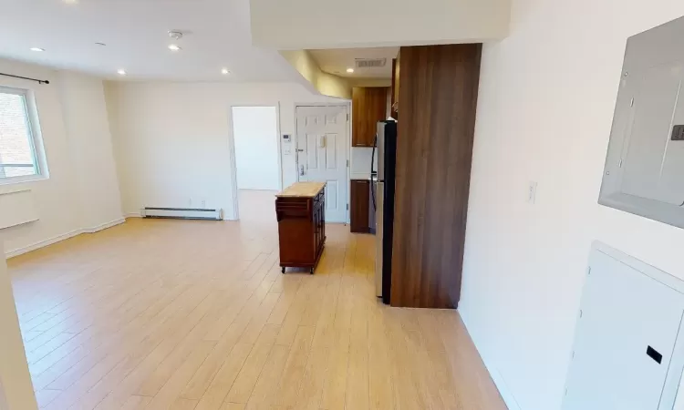 Kitchen with electric panel, a baseboard heating unit, light hardwood / wood-style flooring, a kitchen island, and stainless steel refrigerator