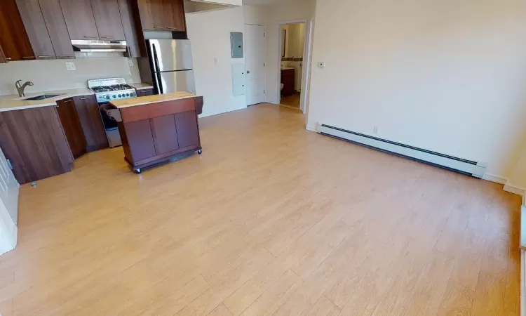 Kitchen featuring gas range, sink, a baseboard heating unit, backsplash, and stainless steel fridge