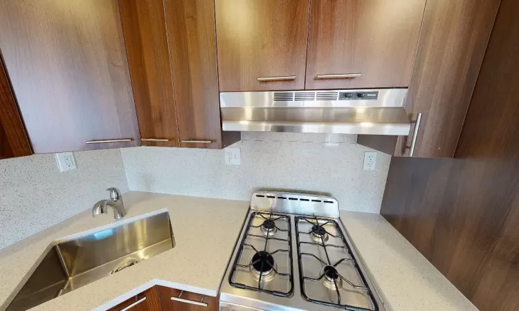 Kitchen with decorative backsplash, sink, extractor fan, and light stone counters