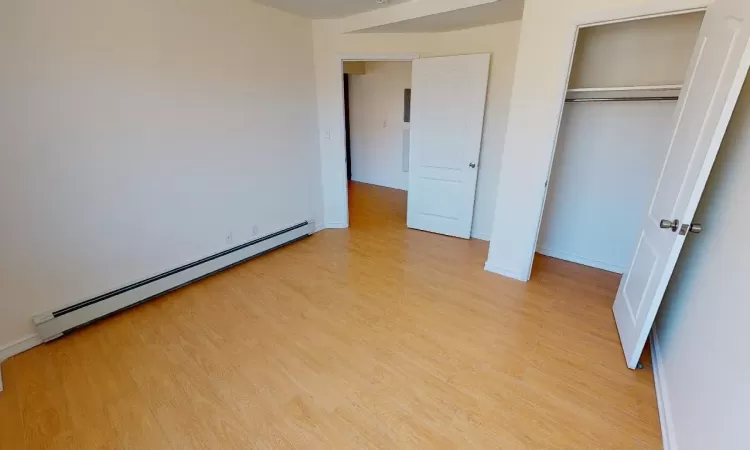 Unfurnished bedroom with a closet, light wood-type flooring, and a baseboard radiator