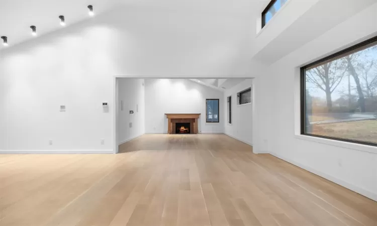 Unfurnished living room featuring high vaulted ceiling, light hardwood / wood-style floors, and a brick fireplace