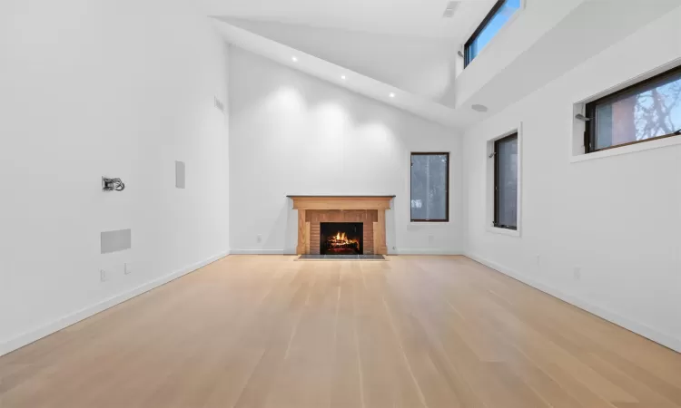 Unfurnished living room with light hardwood / wood-style flooring, a high ceiling, and a brick fireplace