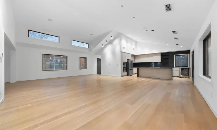 Unfurnished living room featuring a wealth of natural light, a high ceiling, light hardwood / wood-style flooring, and beverage cooler