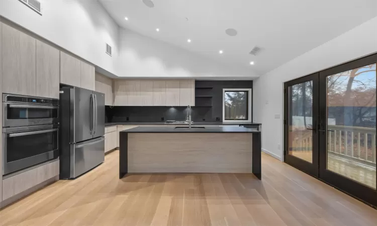 Kitchen featuring french doors, backsplash, stainless steel appliances, sink, and a center island with sink