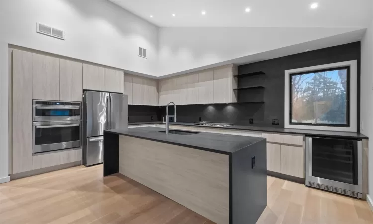 Kitchen featuring sink, beverage cooler, a towering ceiling, an island with sink, and appliances with stainless steel finishes