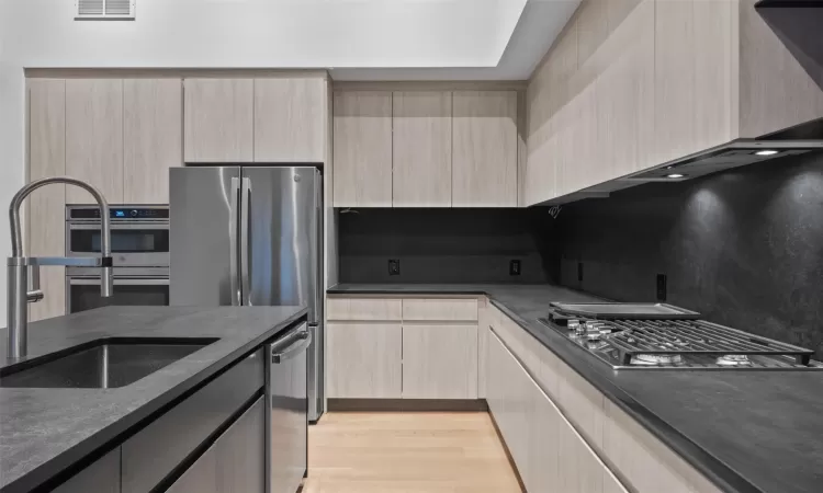 Kitchen with light brown cabinets, sink, stainless steel appliances, decorative backsplash, and light wood-type flooring