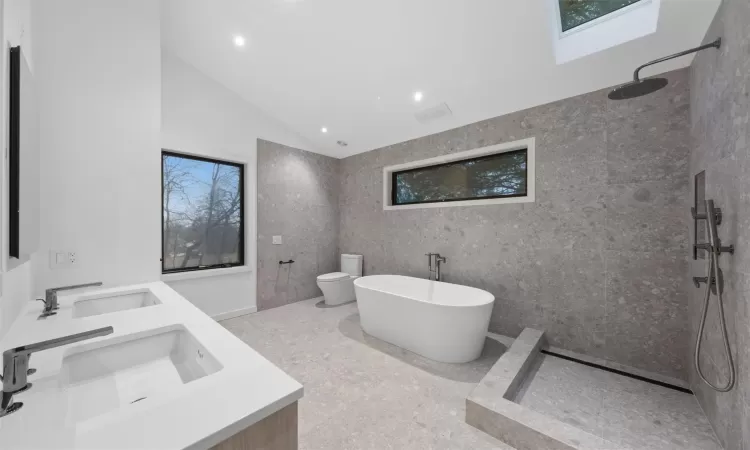 Full bathroom with vanity, lofted ceiling with skylight, separate shower and tub, tile walls, and toilet