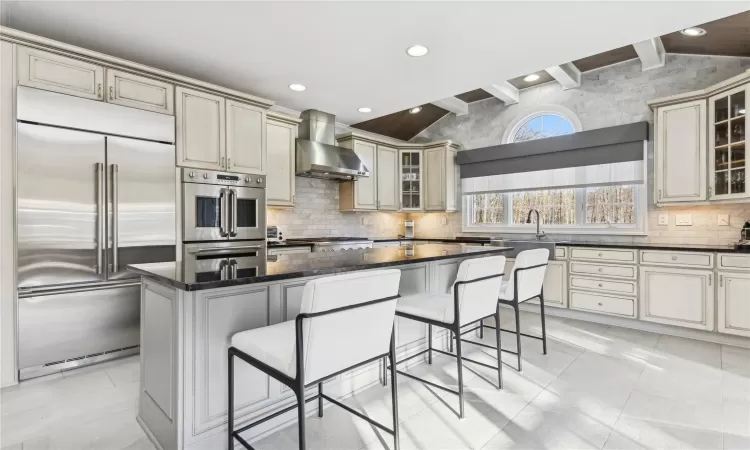 Kitchen with a kitchen breakfast bar, wall chimney range hood, cream cabinetry, a kitchen island, and stainless steel built in refrigerator