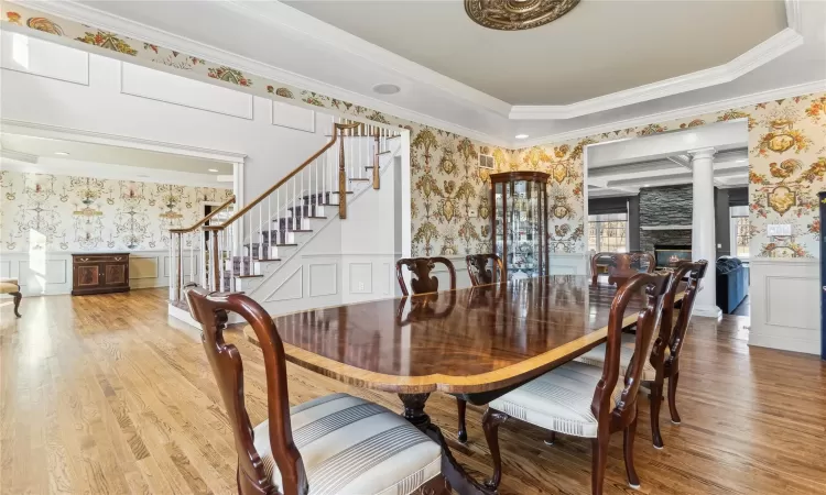 Dining room with wood-type flooring, ornate columns, crown molding, and a stone fireplace