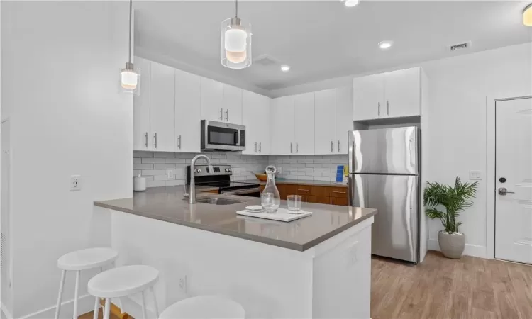 Kitchen featuring pendant lighting, kitchen peninsula, stainless steel appliances, and white cabinetry