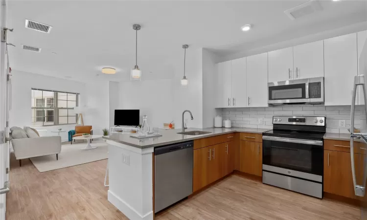 Kitchen with sink, appliances with stainless steel finishes, tasteful backsplash, decorative light fixtures, and white cabinetry