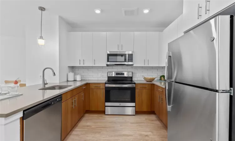 Kitchen featuring sink, hanging light fixtures, stainless steel appliances, backsplash, and white cabinets