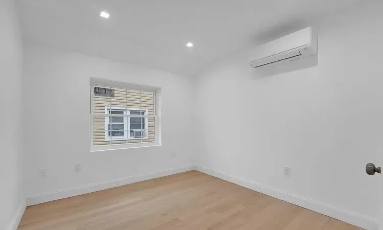 Unfurnished room featuring a wall mounted air conditioner and light hardwood / wood-style flooring