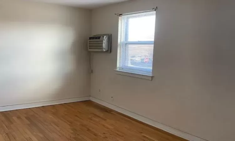 Unfurnished room featuring hardwood / wood-style flooring and a wall unit AC