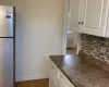 Kitchen with backsplash, dark wood-type flooring, white cabinets, radiator heating unit, and stainless steel refrigerator