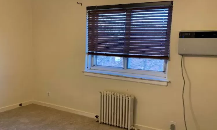 Carpeted spare room featuring a wall mounted AC, plenty of natural light, and radiator