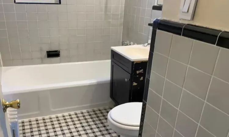 Bathroom with tile patterned floors, vanity, toilet, and tile walls