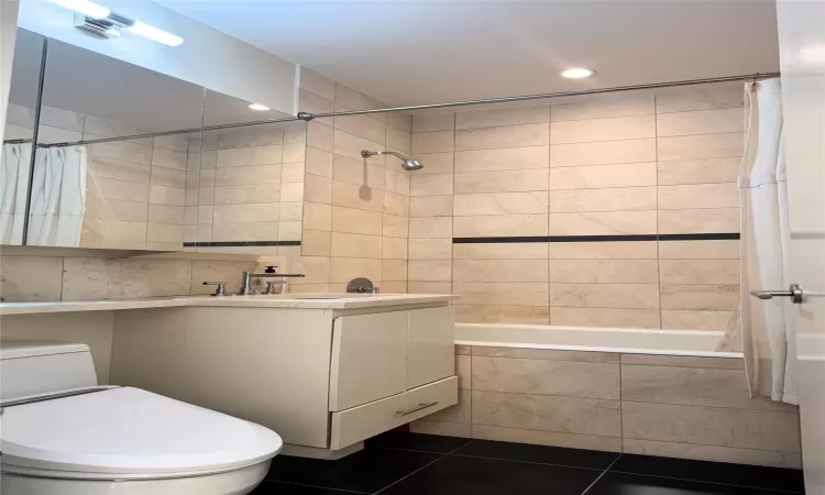 Full bathroom featuring shower / tub combo, tile patterned floors, vanity, tile walls, and toilet