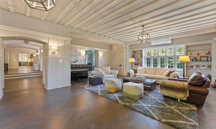 Living room with a wall mounted air conditioner, dark parquet floors, and a chandelier