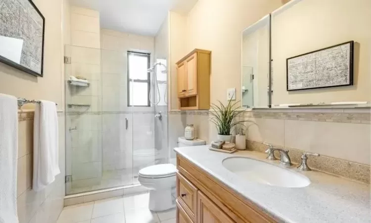 Bathroom with tile patterned floors, toilet, a shower with door, vanity, and tile walls