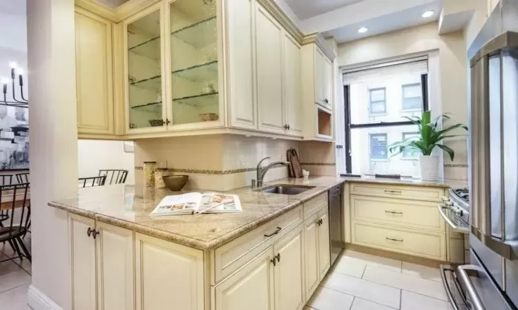 Kitchen featuring cream cabinetry, light stone counters, light tile patterned floors, and sink