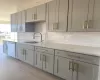 Kitchen featuring dishwasher, sink, light stone counters, backsplash, and gray cabinets