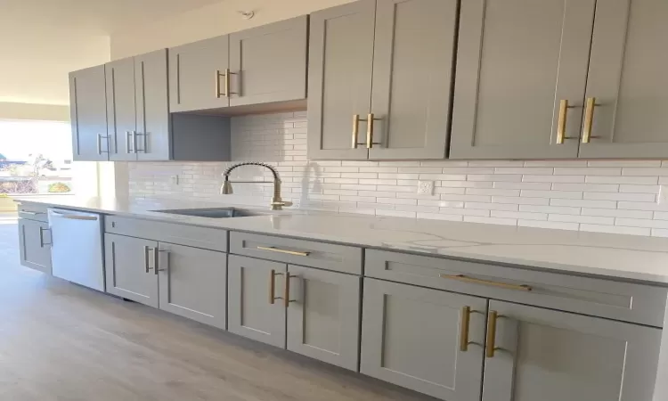 Kitchen featuring dishwasher, sink, light stone counters, backsplash, and gray cabinets