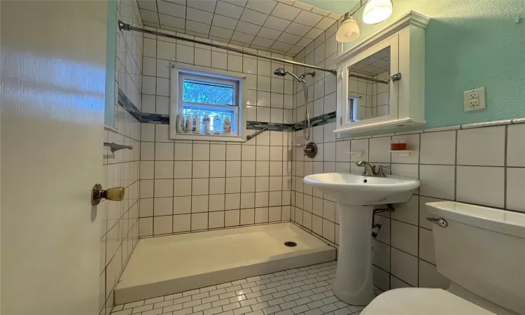 Bathroom featuring tile patterned flooring, toilet, tiled shower, decorative backsplash, and tile walls