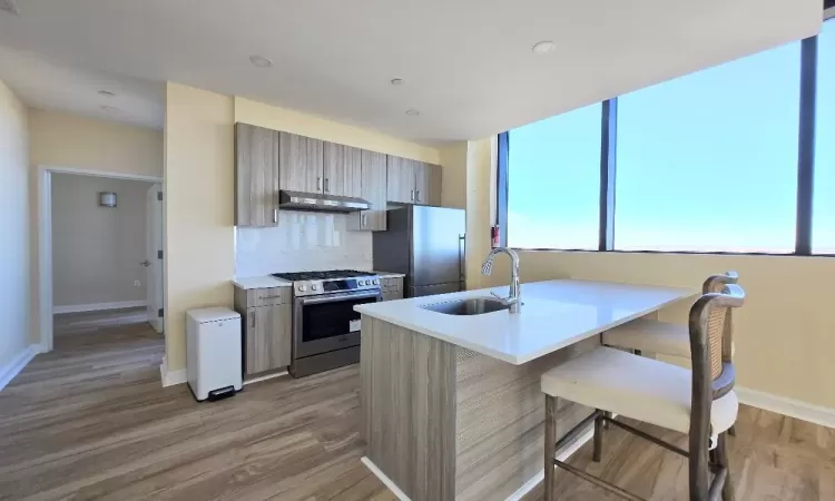 Kitchen featuring sink, stainless steel appliances, light hardwood / wood-style floors, a breakfast bar, and exhaust hood