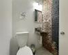 Bathroom featuring toilet, sink, and brick wall