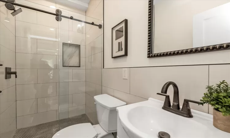 Bathroom with walk in shower, toilet, tile walls, and sink