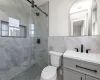 Bathroom featuring walk in shower, vanity, toilet, and tile walls