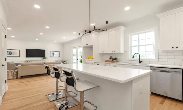 Kitchen with sink, stainless steel dishwasher, a kitchen island, light stone counters, and white cabinetry