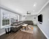 Living room featuring dark wood-type flooring, ceiling fan, and crown molding