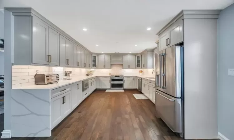 Kitchen featuring backsplash, gray cabinets, dark wood-type flooring, and appliances with stainless steel finishes