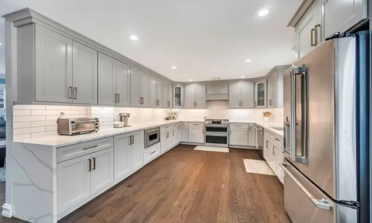 Kitchen featuring light stone countertops, dark hardwood / wood-style flooring, gray cabinetry, custom exhaust hood, and stainless steel appliances