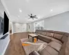 Living room with ceiling fan, dark wood-type flooring, and ornamental molding