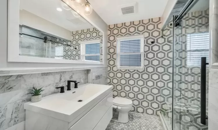 Bathroom featuring tile patterned flooring, vanity, toilet, and a shower with door