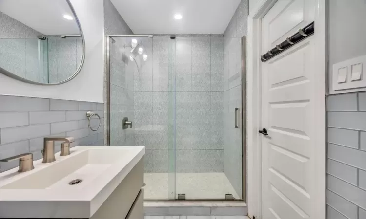 Bathroom featuring vanity, an enclosed shower, decorative backsplash, and tile walls