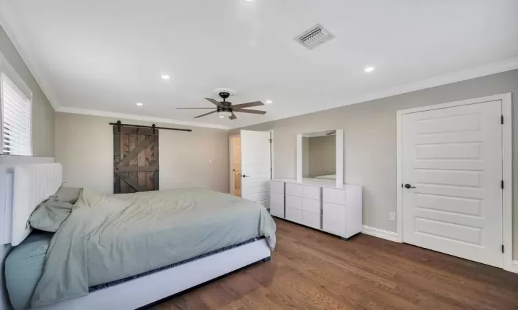 Bedroom with a barn door, ceiling fan, crown molding, and dark wood-type flooring