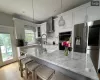 Kitchen with light stone countertops, appliances with stainless steel finishes, wall chimney exhaust hood, decorative light fixtures, and white cabinetry