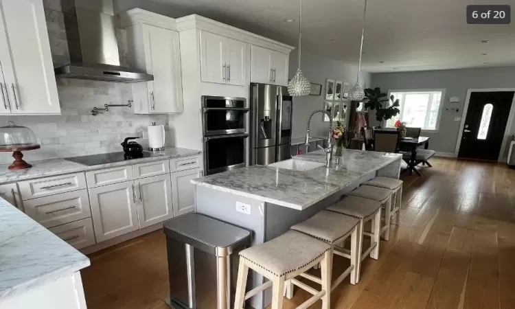 Kitchen with white cabinetry, a kitchen island with sink, black appliances, and wall chimney range hood