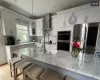 Kitchen featuring pendant lighting, wall chimney range hood, appliances with stainless steel finishes, tasteful backsplash, and white cabinetry