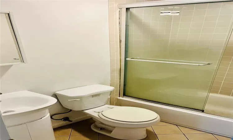 Full bathroom with toilet, vanity, tile patterned floors, and bath / shower combo with glass door