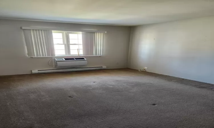 Carpeted spare room featuring baseboard heating and an AC wall unit