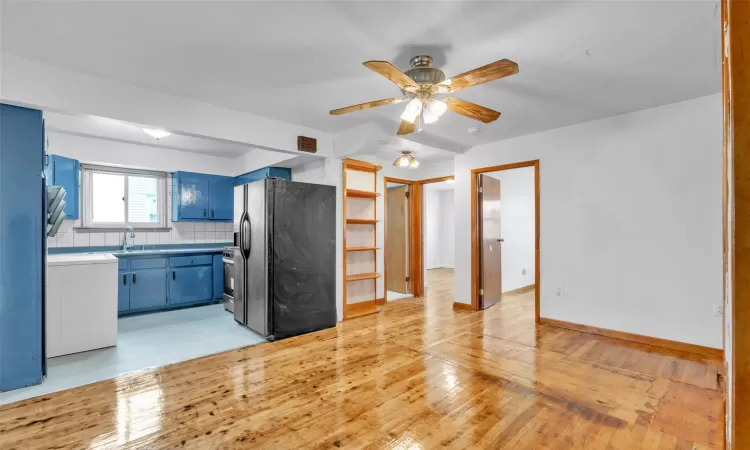 Kitchen featuring ceiling fan, black fridge, blue cabinets, backsplash, and light hardwood / wood-style floors