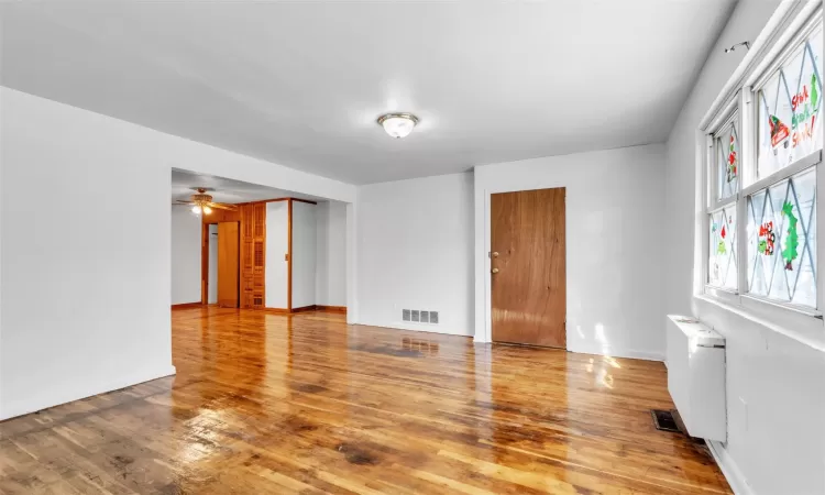 Empty room featuring ceiling fan, wood-type flooring, and radiator heating unit